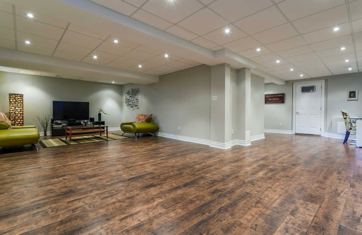 Modern basement renovation with wood-look flooring, recessed lighting, and a stylish entertainment area featuring contemporary green furniture and neutral walls. Ideal for family gatherings and relaxation.