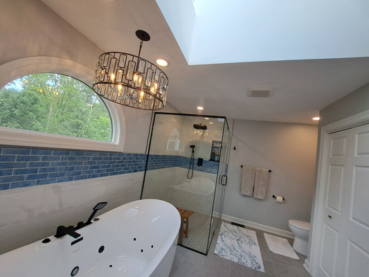 Finished master bathroom remodel with freestanding soaking tub, curbless glass shower, blue accent tile band, and skylight for natural light