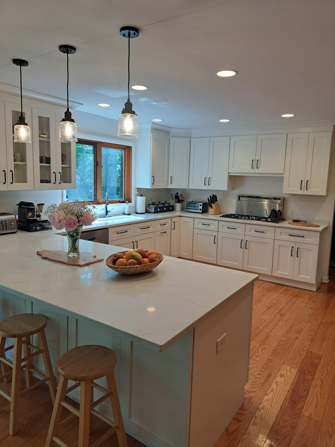 Modern white shaker kitchen with oversized island, quartz countertops, glass pendant lights, and natural wood flooring