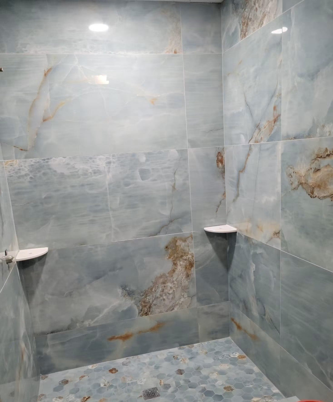 Blue large-format tile shower with hexagon mosaic floor, coordinated grout lines, and corner shelves.