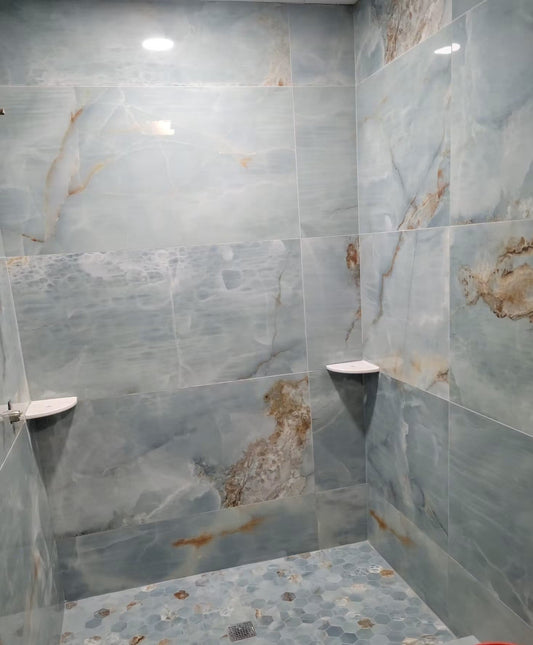 Blue large-format tile shower with hexagon mosaic floor, coordinated grout lines, and corner shelves.