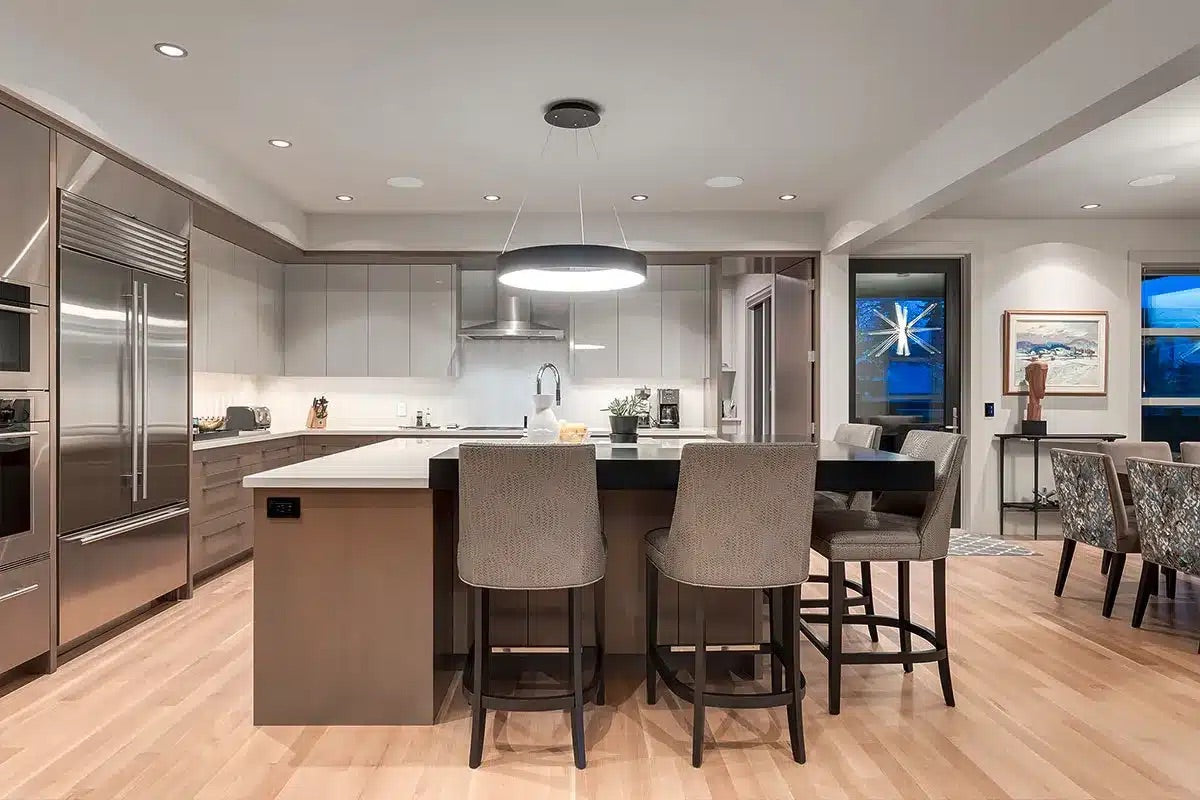 Modern open-concept kitchen with grey flat-panel cabinets, large center island, circular pendant light, stainless steel appliances, and hardwood floors
