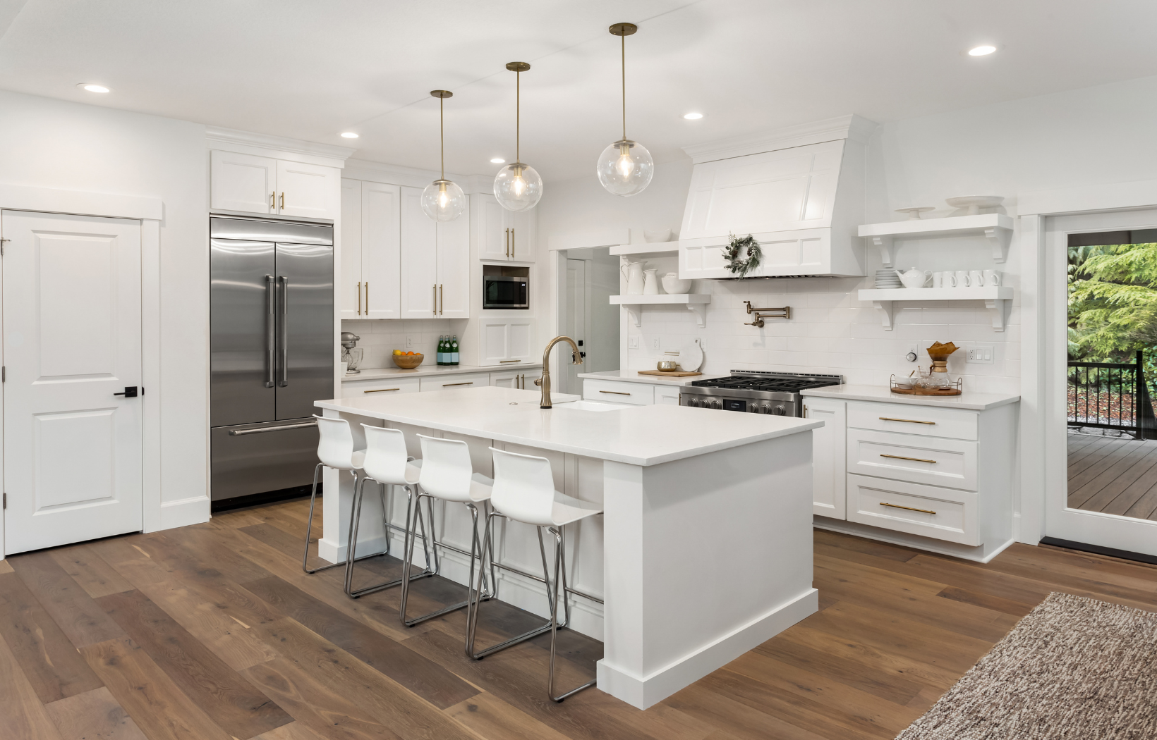 White shaker kitchen with custom range hood, open shelving, brass hardware, glass globe pendants, white quartz island, and dark hardwood floors
