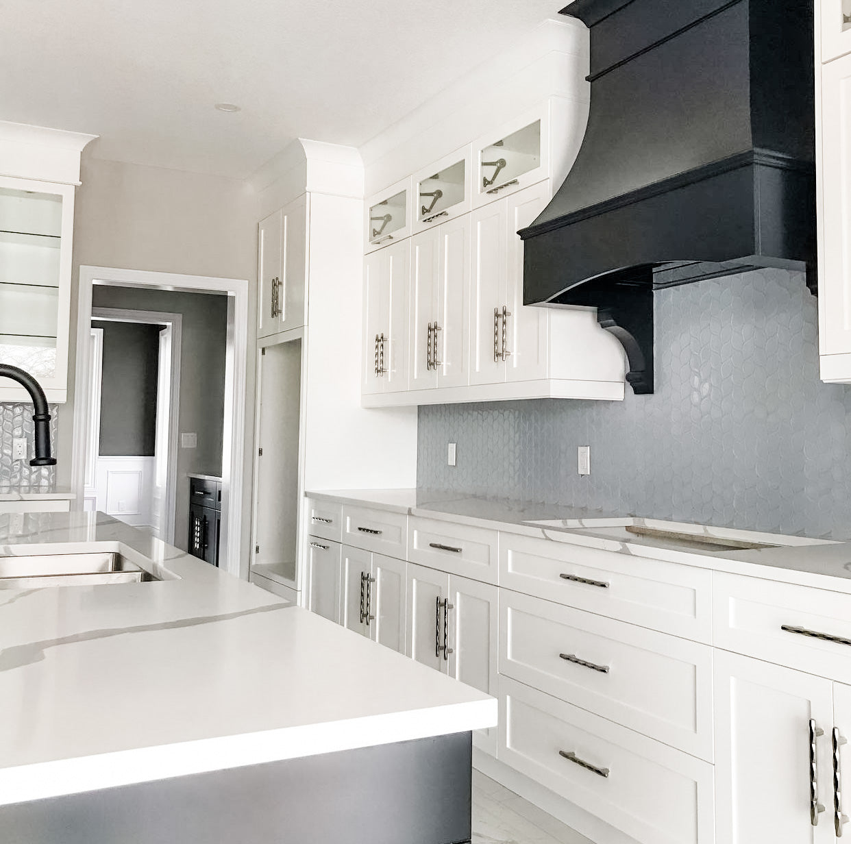 Modern kitchen with white cabinets, black range hood, and gray backsplash