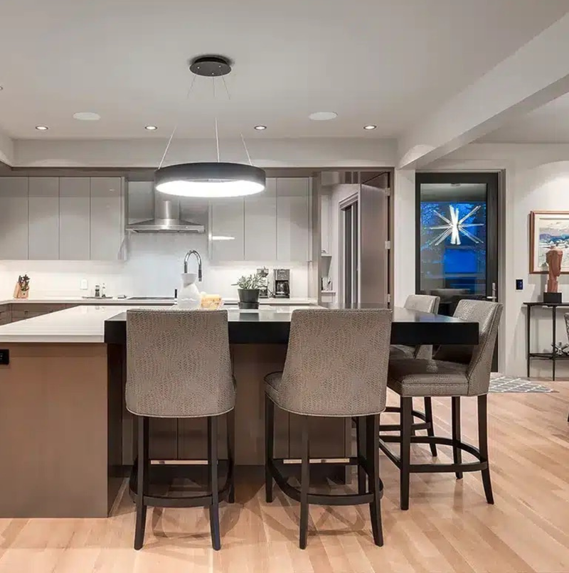 Modern kitchen with grey flat-panel cabinets, a waterfall-edge island with bar seating, statement ring pendant light, and light hardwood floors