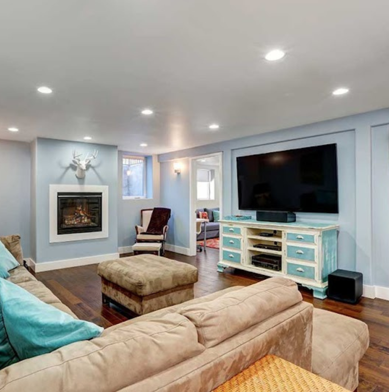 Finished basement living space with a gas fireplace, wall-mounted TV, sectional sofa, recessed lighting, and dark hardwood floors