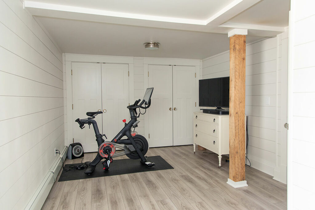 Home gym with stationary bike and TV in a room with wooden flooring and white walls