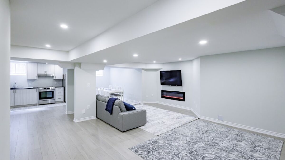 Modern living room with gray sofa, TV, and kitchen in a well-lit basement